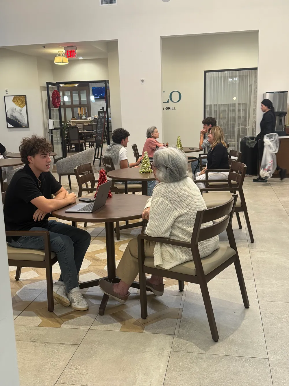 A SAGE student sitting at a table in The Contemporary's common room, talking with a resident in a white sweater