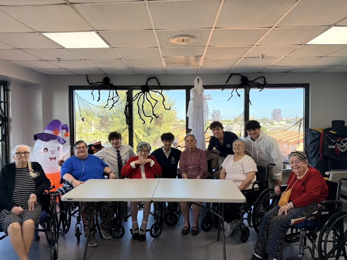 SAGE students gathered around a table with residents at Waterford, in a room decorated for Halloween